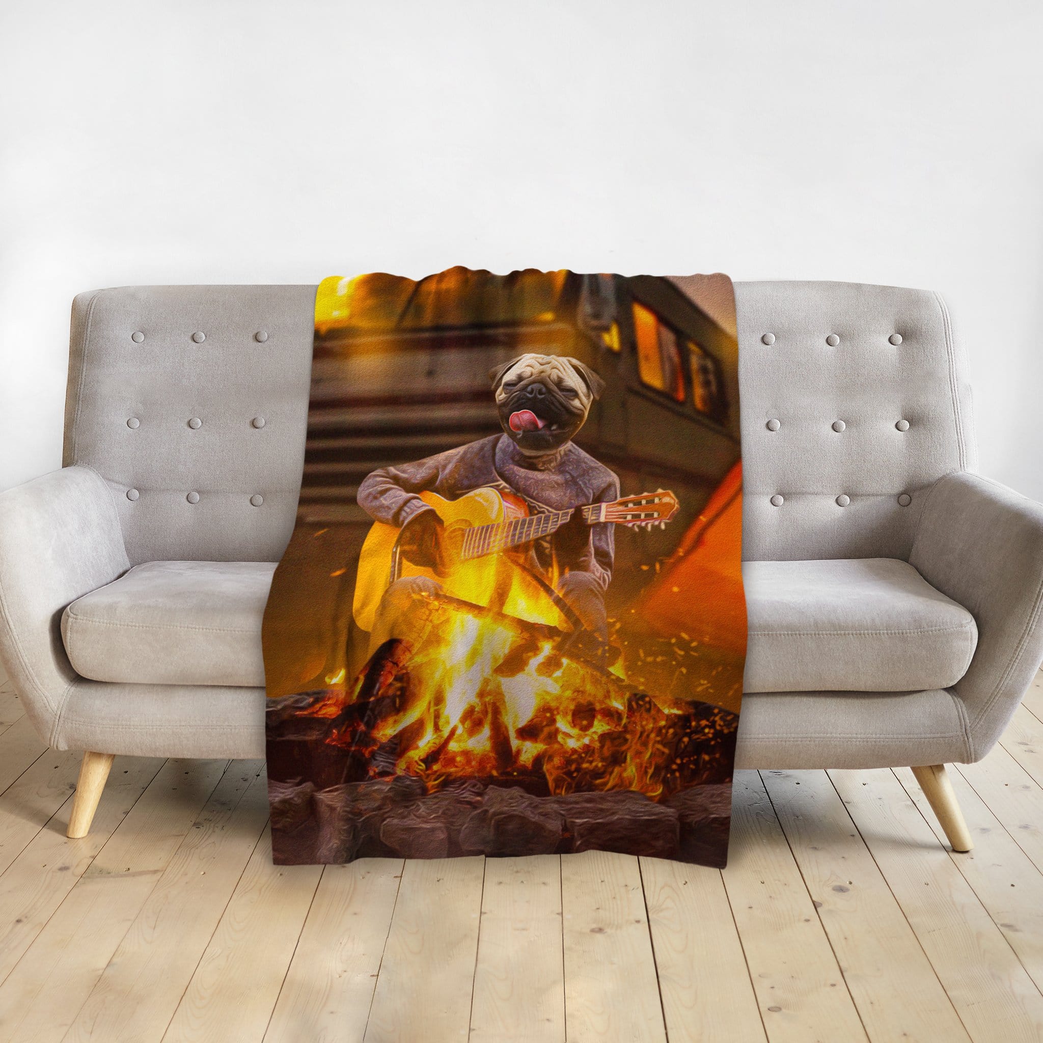 Personalized pet blanket with a pug playing guitar by a campfire, draped over a gray sofa.
