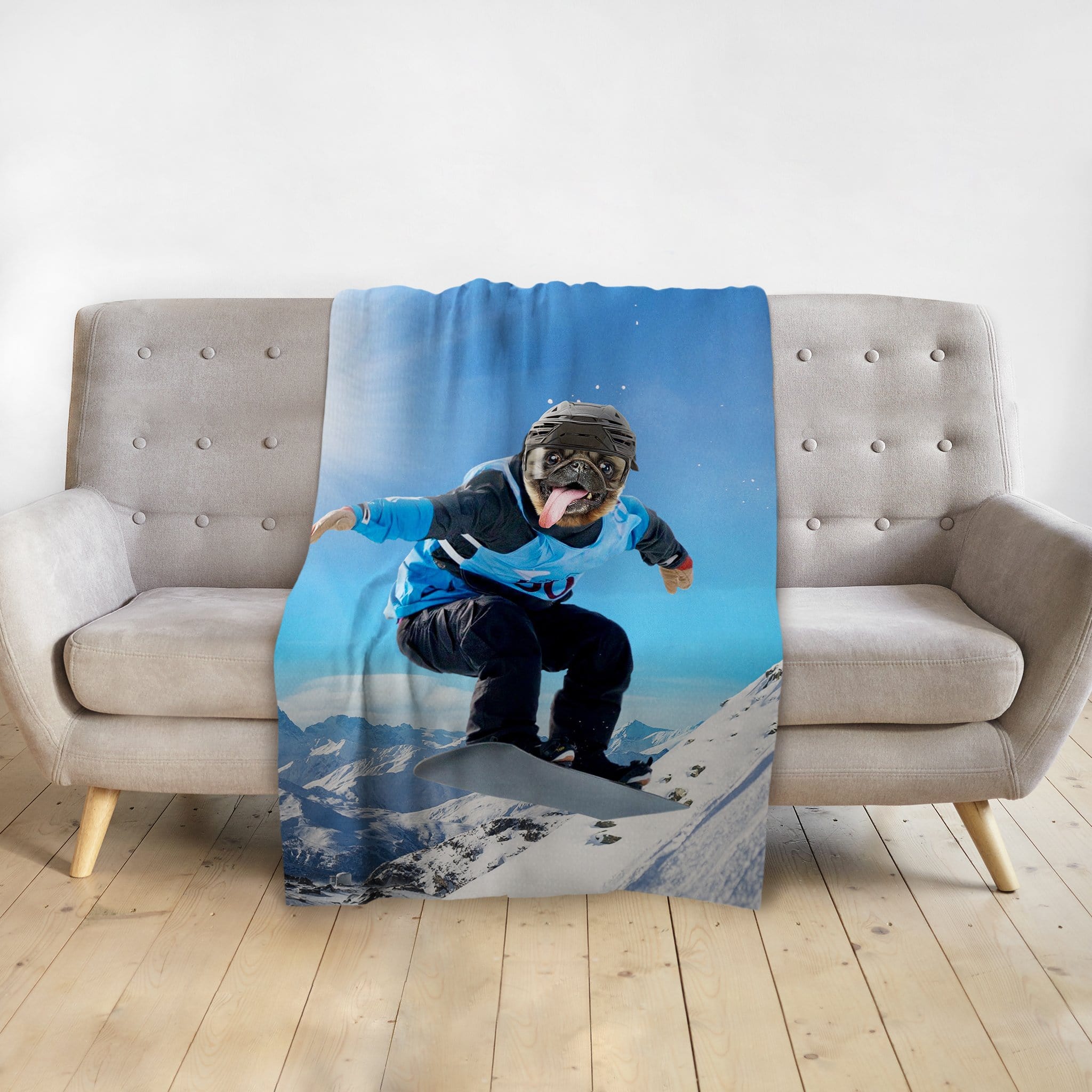 Personalized pet blanket with a pug's head on a snowboarder's body, draped over a gray sofa.